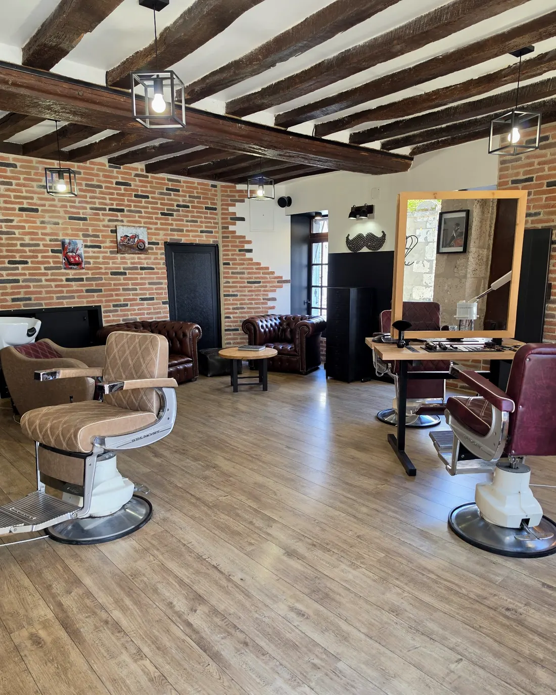 La salle du salon : poutres, briques, fauteuils Chesterfield et fauteuils de barbier Belmont