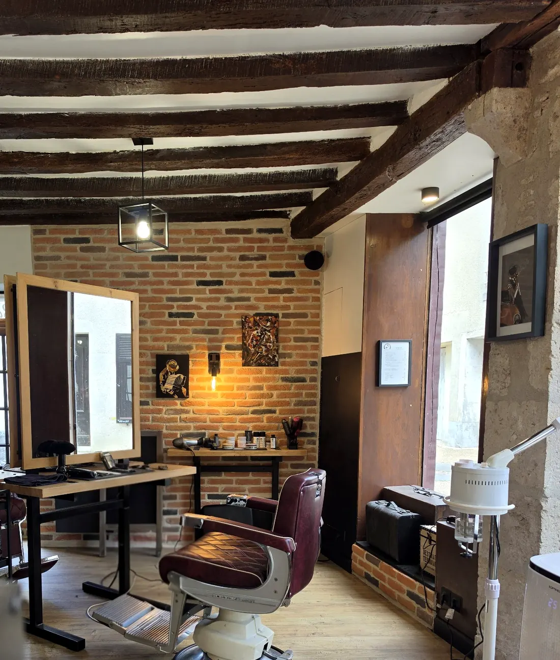 Un poste de barbier avec fauteuil bordeaux, miroir en chêne et mur de briques